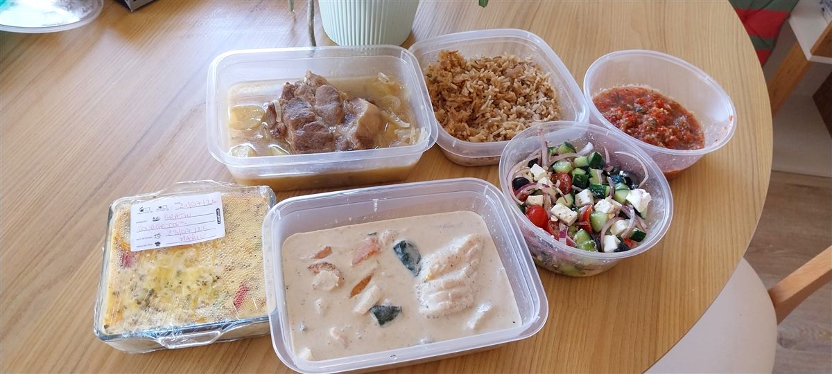 Six boîtes de repas maison préparées pendant une session : rôti aux oignons, riz, salade grecque, gratin de courgettes, poisson à la crème et sauce tomate